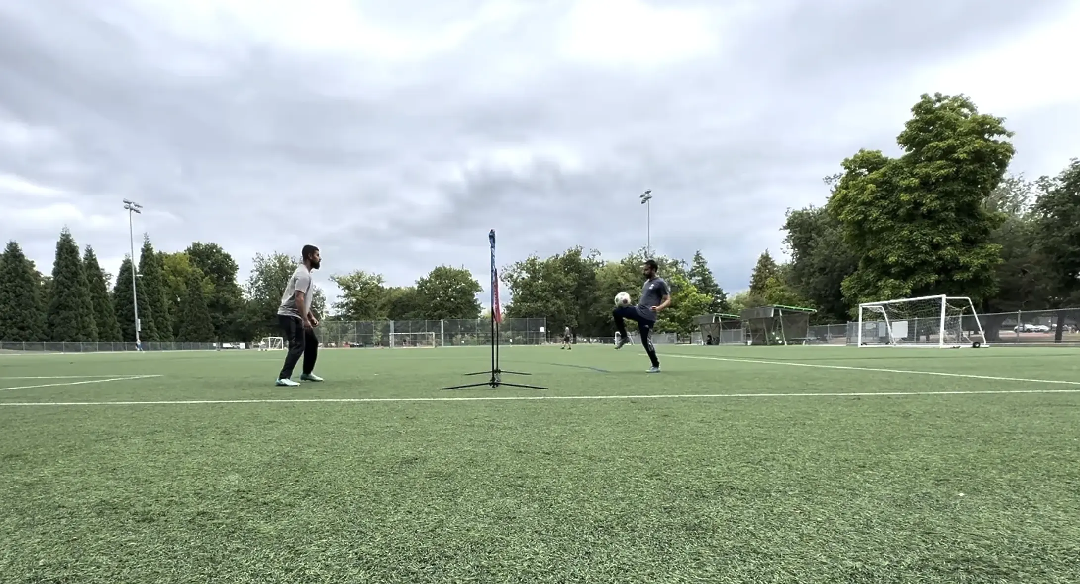 Two young players playing soccer tennis over a net on a field